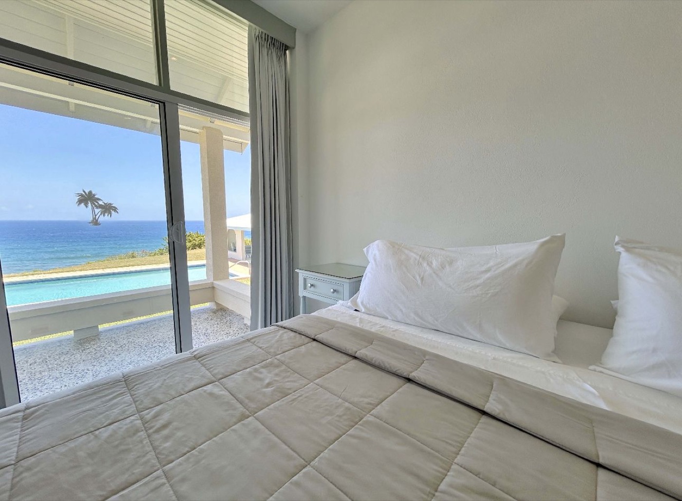 Bedroom with a white bed and sliding doors opening toward the ocean